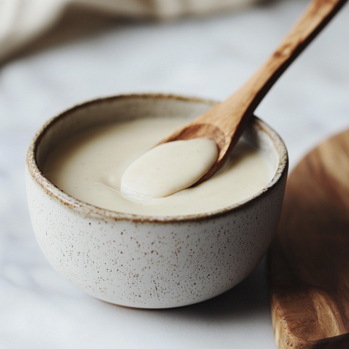 Béchamel vegan onctueuse dans un bol en céramique, texture lisse et crémeuse, cuillère en bois